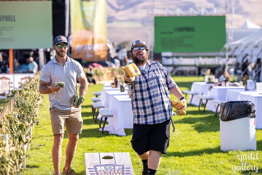 Two men are playing a game of cornhole in a field.