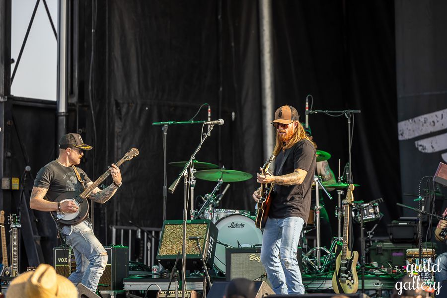 Two men are playing guitars and banjo on a stage.