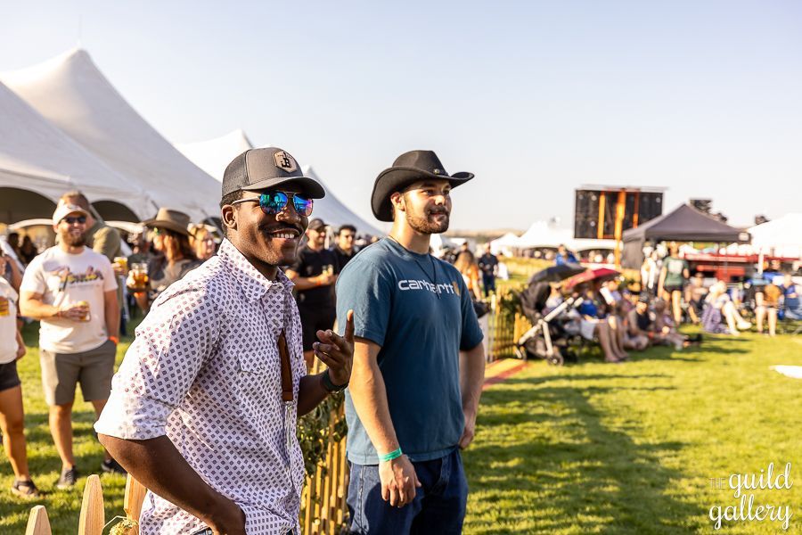 Two men are standing next to each other in a field at a festival.