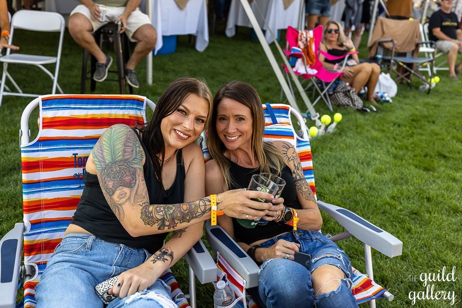 Two women are sitting in lawn chairs holding drinks.