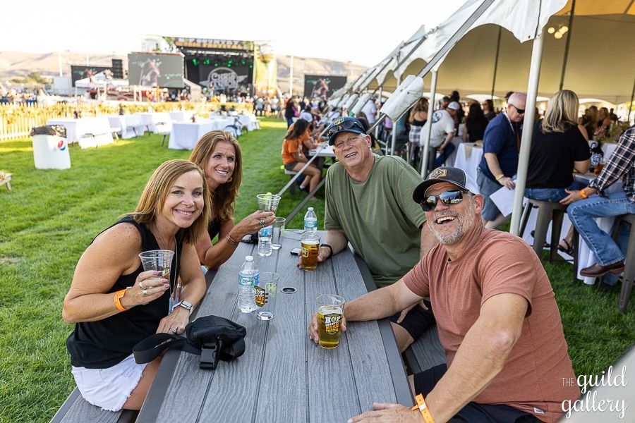 A group of people are sitting at a picnic table drinking beer.