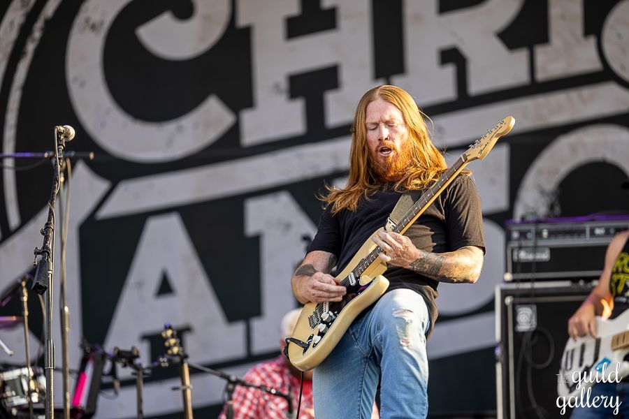 A man with long red hair is playing a guitar on stage