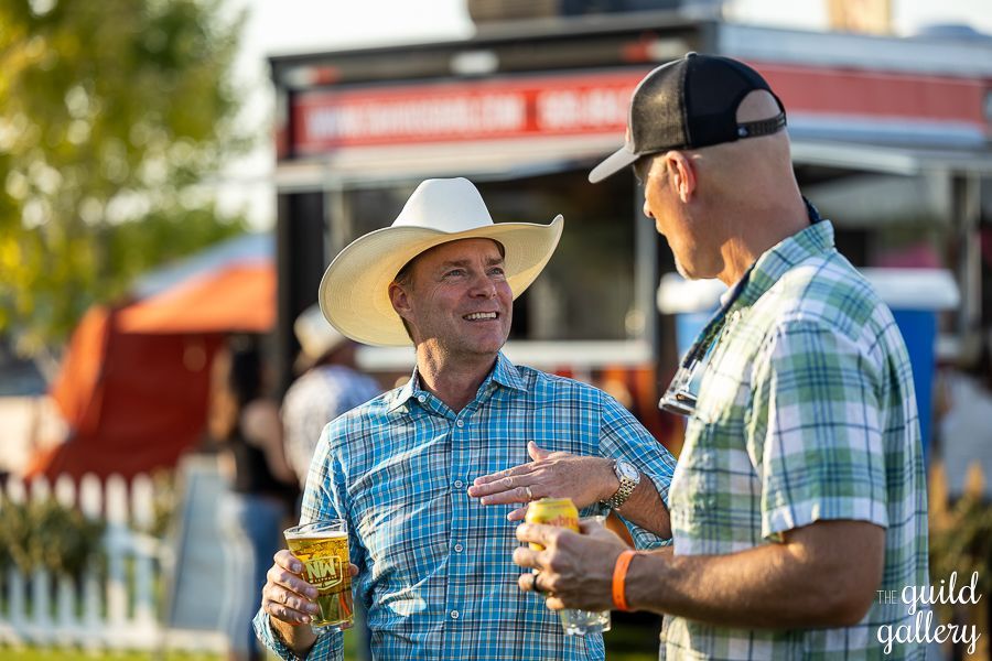 Two men in cowboy hats are talking to each other while holding beer.