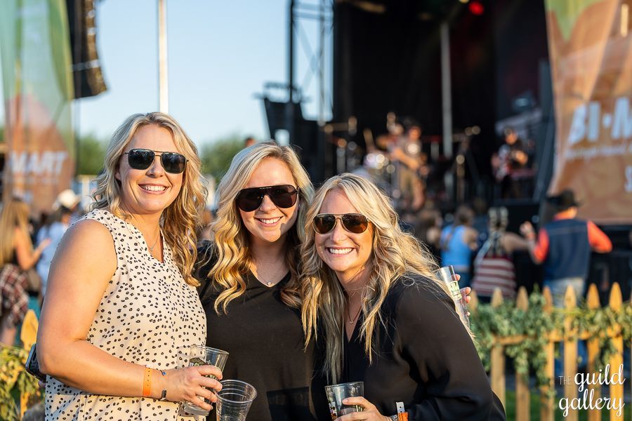 Three women wearing sunglasses are posing for a picture at a concert.