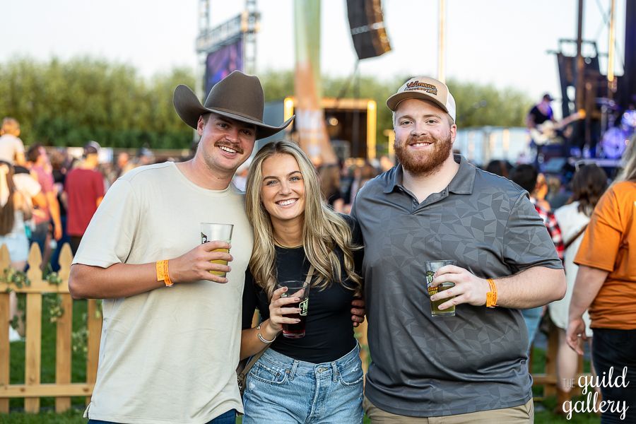 Three people are posing for a picture at a concert while holding drinks.
