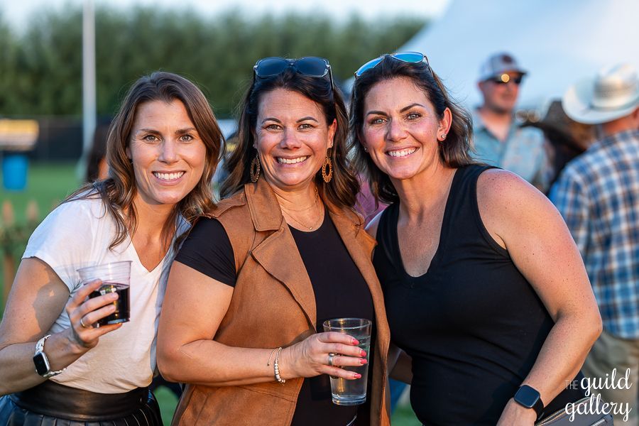 Three women are posing for a picture together while holding drinks.