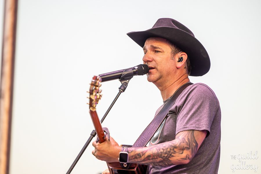 A man in a cowboy hat is singing into a microphone while playing a guitar.