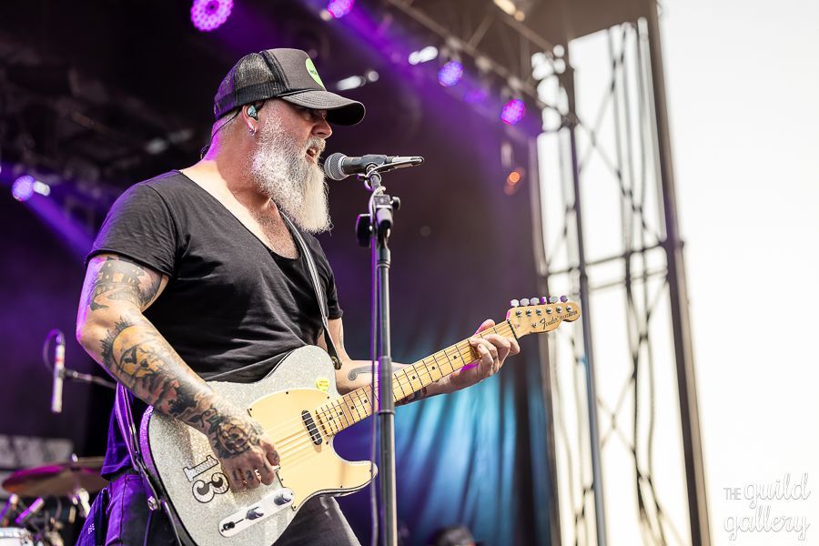 A man with a beard is playing a guitar and singing into a microphone on a stage.