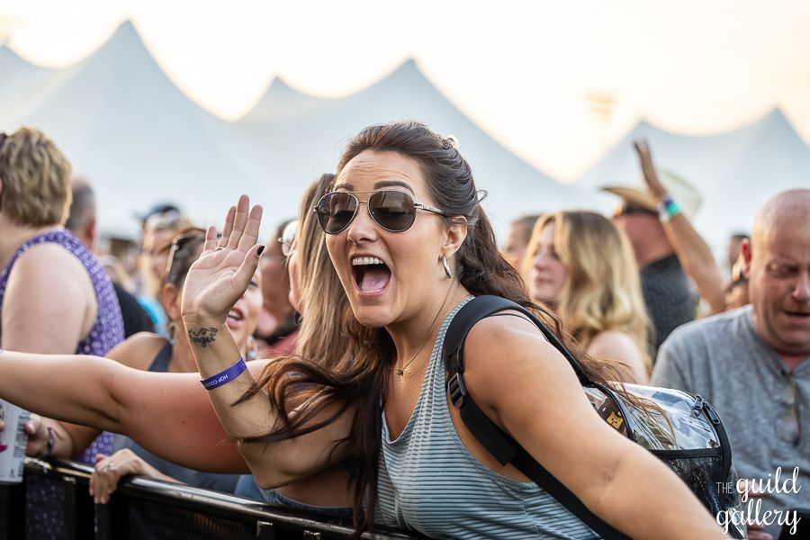 A woman wearing sunglasses is standing in a crowd of people at a concert.