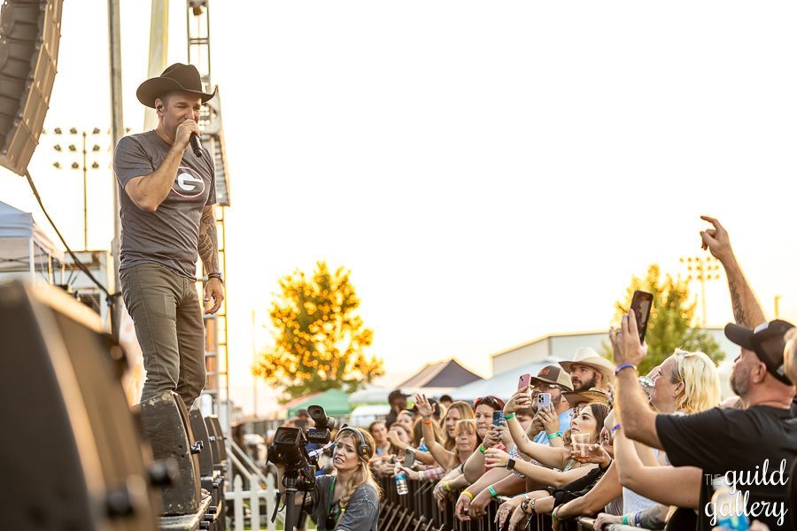 A man in a cowboy hat is singing into a microphone in front of a crowd of people.