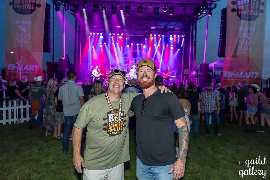 Two men are posing for a picture in front of a stage at a concert.