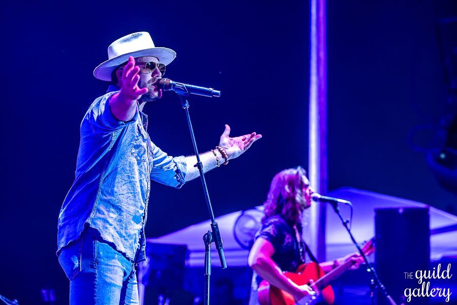 A man is singing into a microphone while another man plays a guitar on stage.