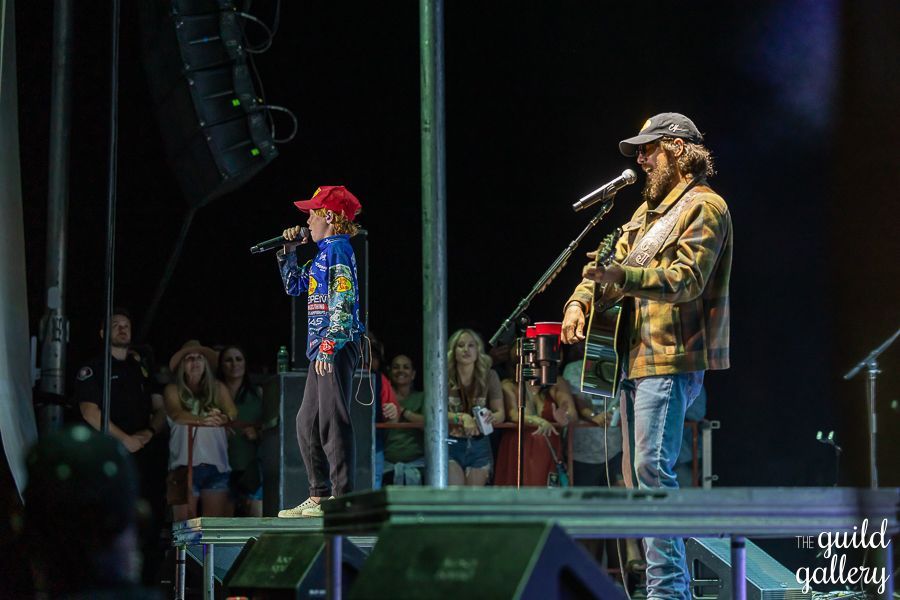 A man is playing a guitar and a boy is singing into a microphone on a stage.