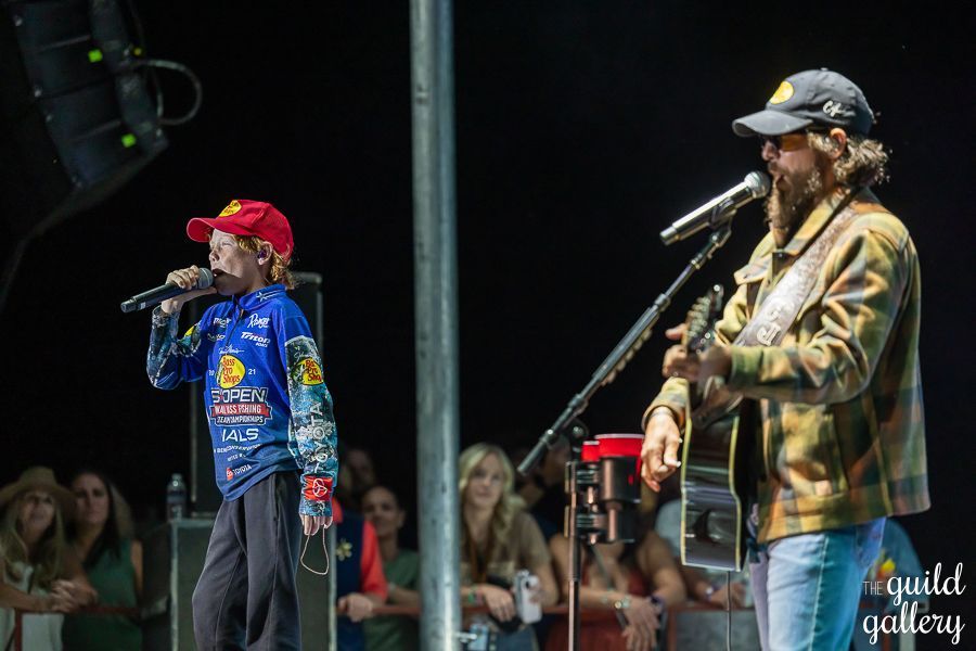 A man is singing into a microphone while another man plays a guitar on stage.