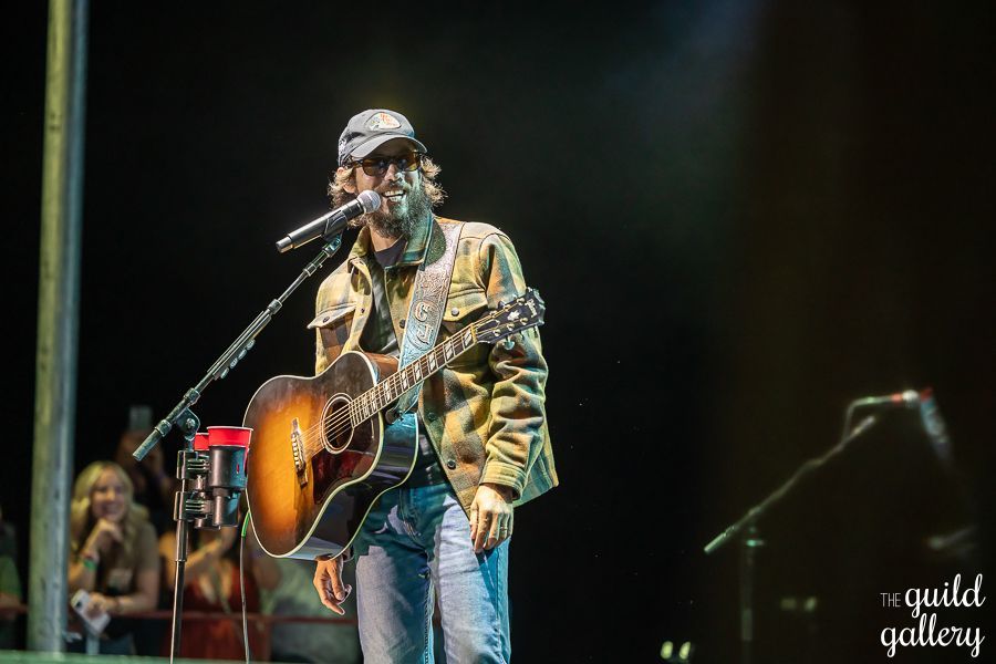A man is playing a guitar and singing into a microphone on a stage.