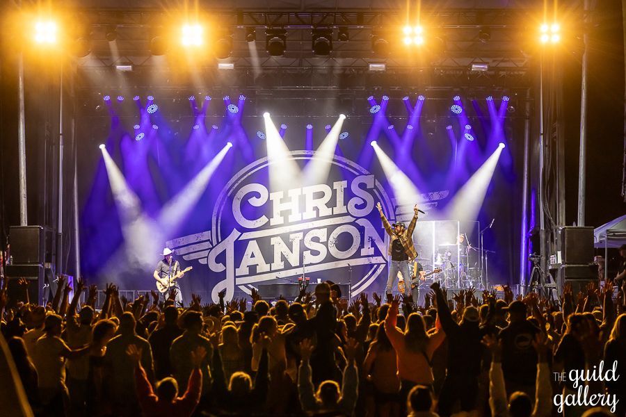 A crowd of people are standing in front of a stage at a chris janson concert.
