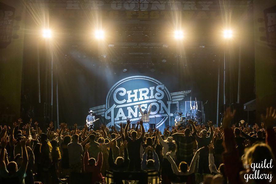 A crowd of people are watching chris janson perform on stage.