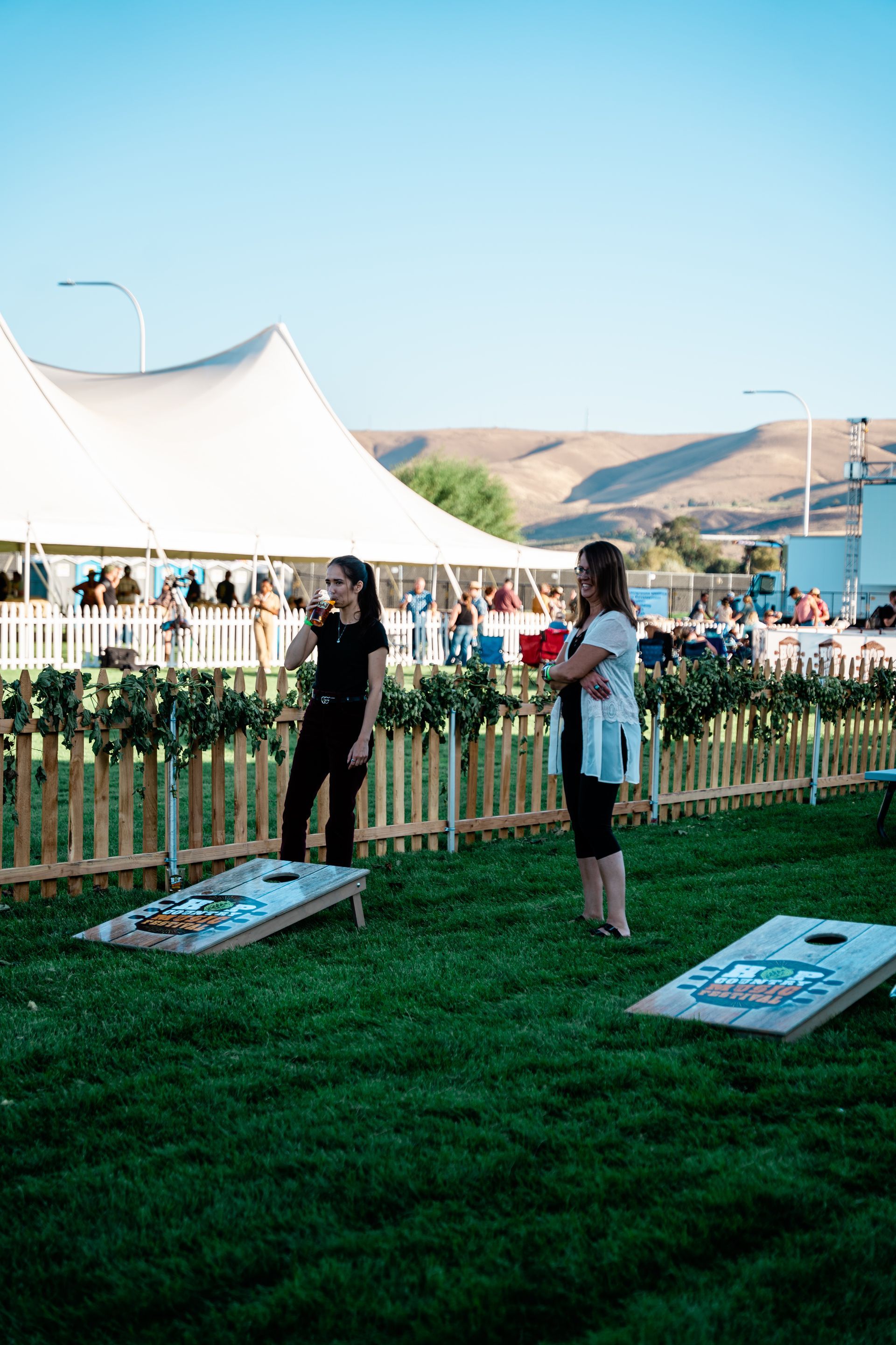 Two women are playing cornhole in a grassy field.