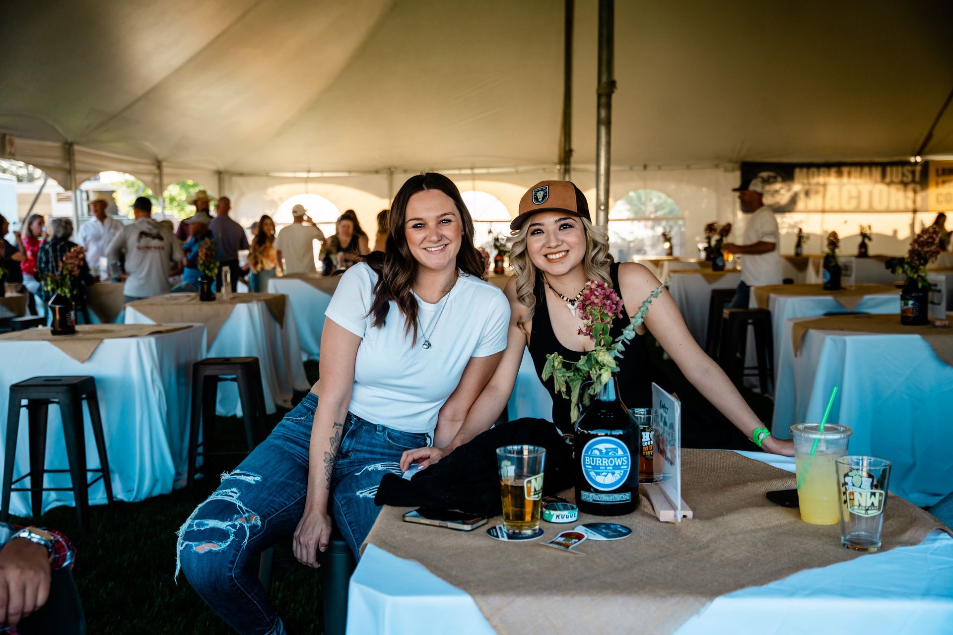 Two women are sitting at a table under a tent.