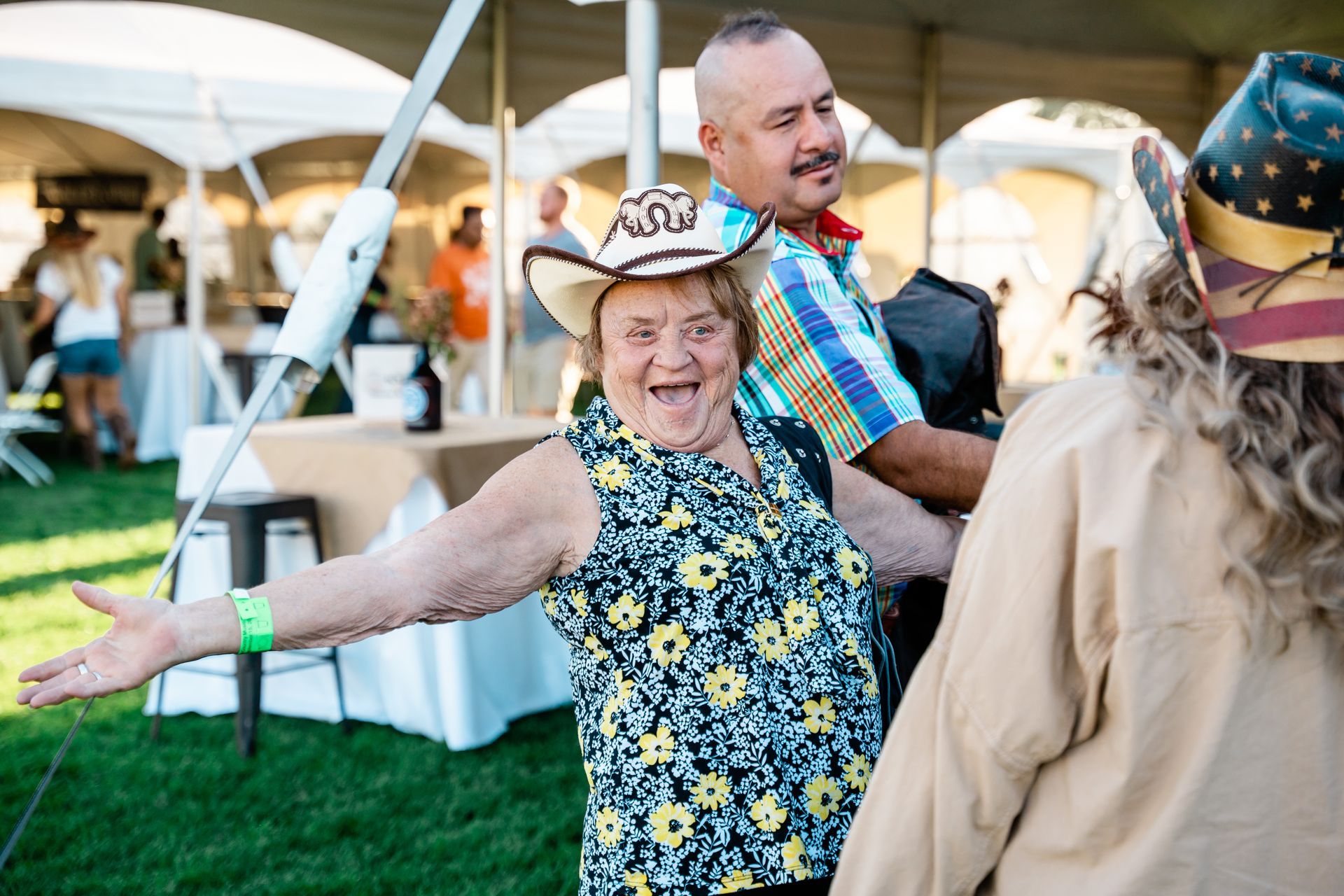 A woman wearing a cowboy hat is standing in a field with her arms outstretched.
