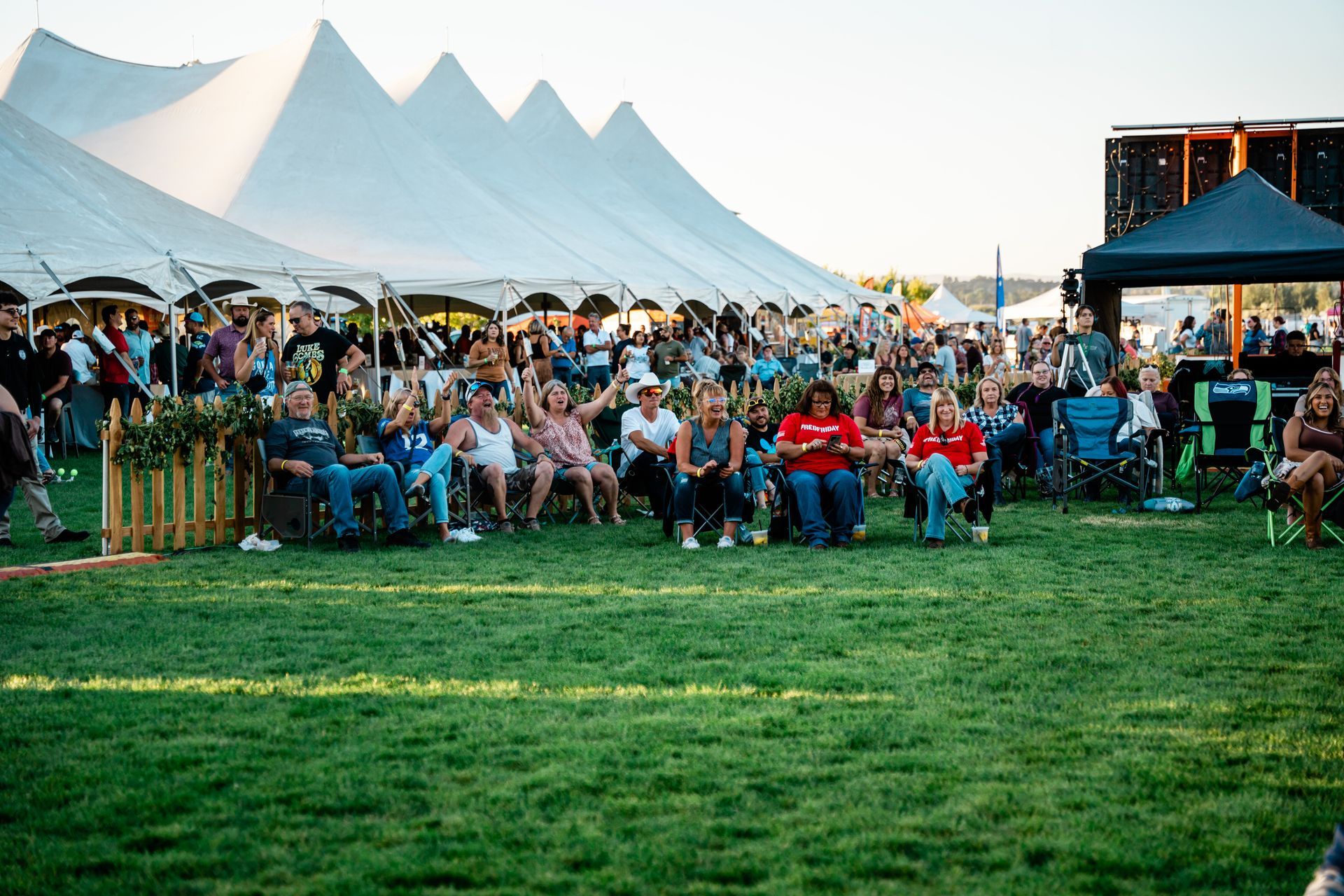 A large group of people are sitting in chairs in front of a large tent.