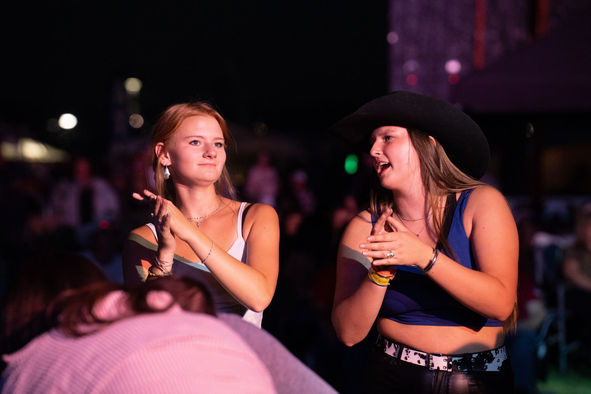 Two women are standing next to each other at a concert . one of the women is wearing a cowboy hat.