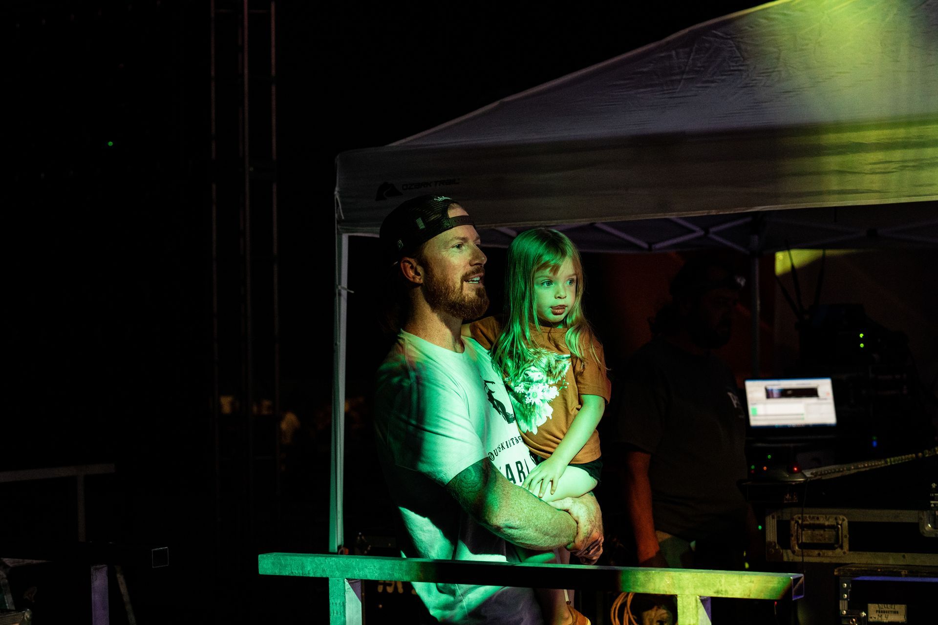 A man is holding a little girl in his arms at a concert.