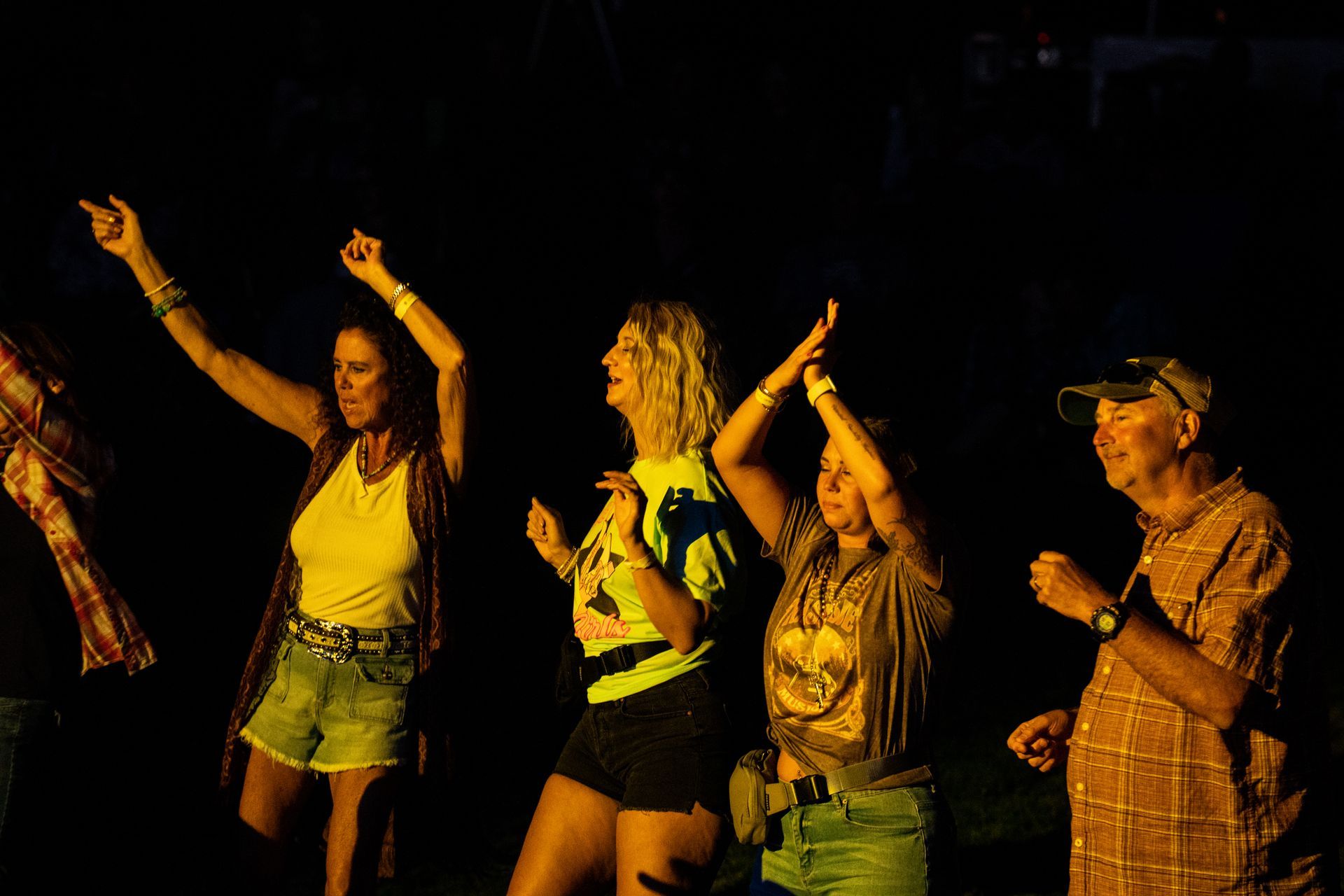 A group of people are dancing in the dark with their arms in the air.