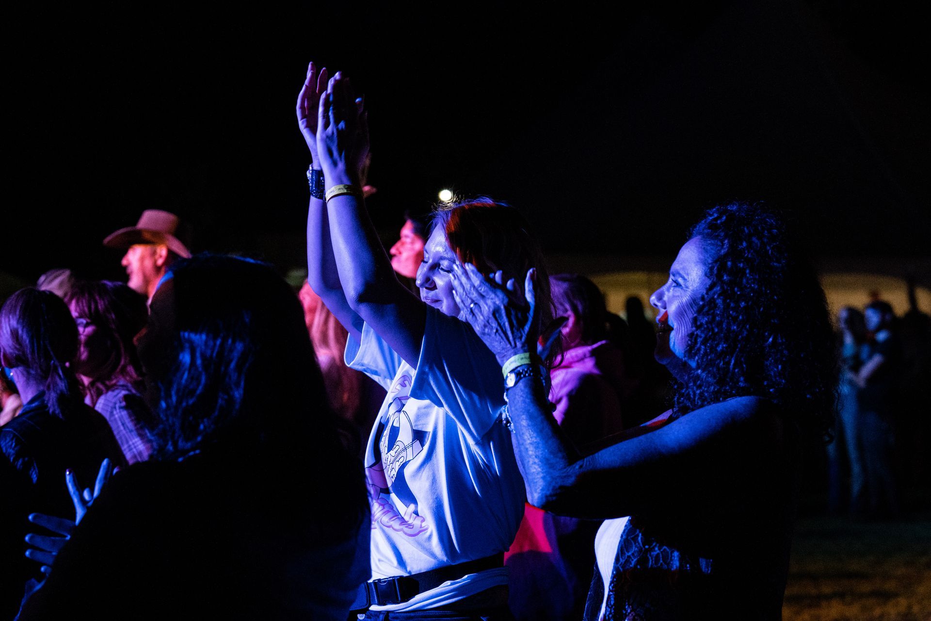 A group of people are standing in a dark room with their hands in the air.