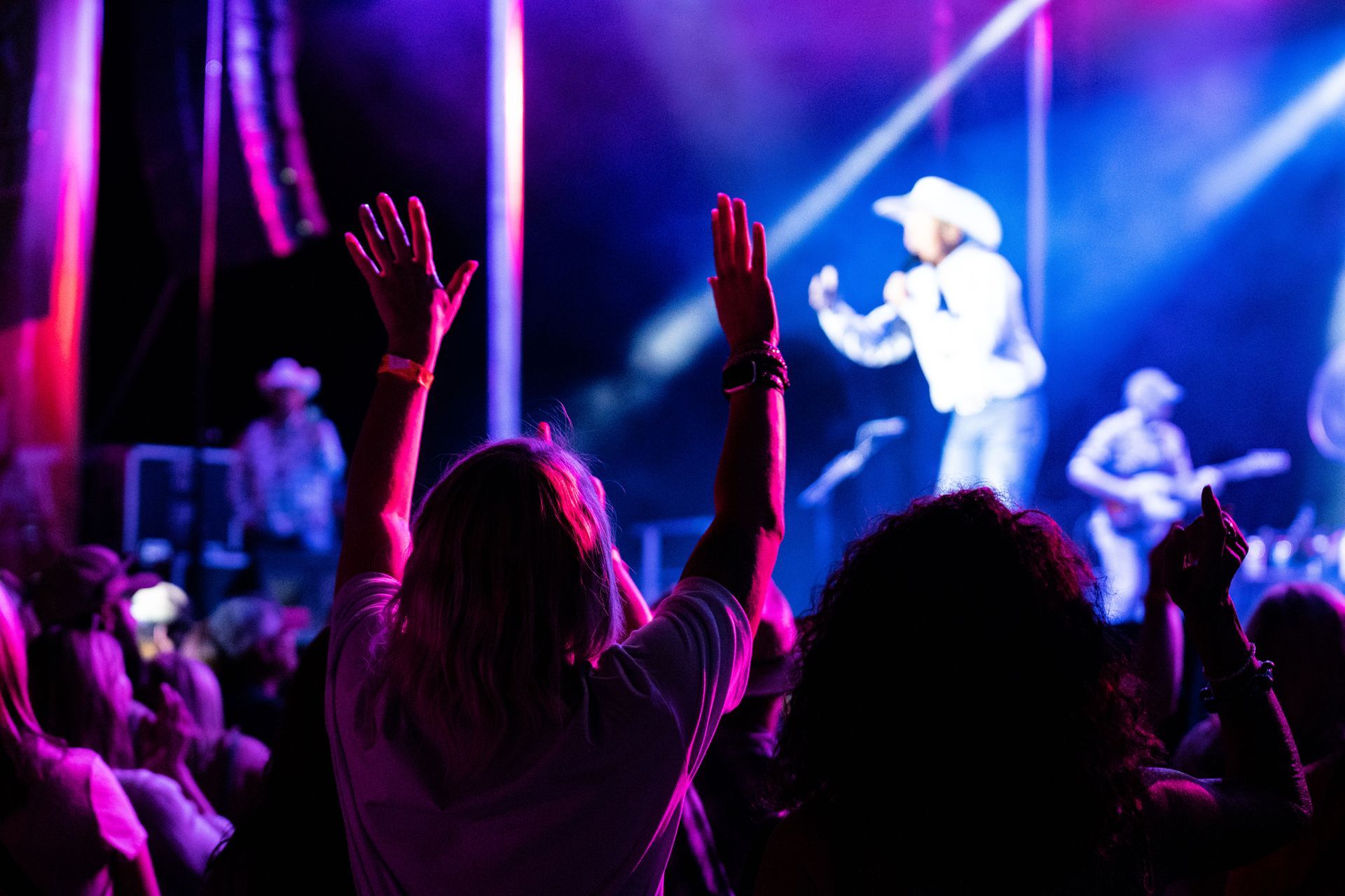A crowd of people are watching a concert with their hands in the air.