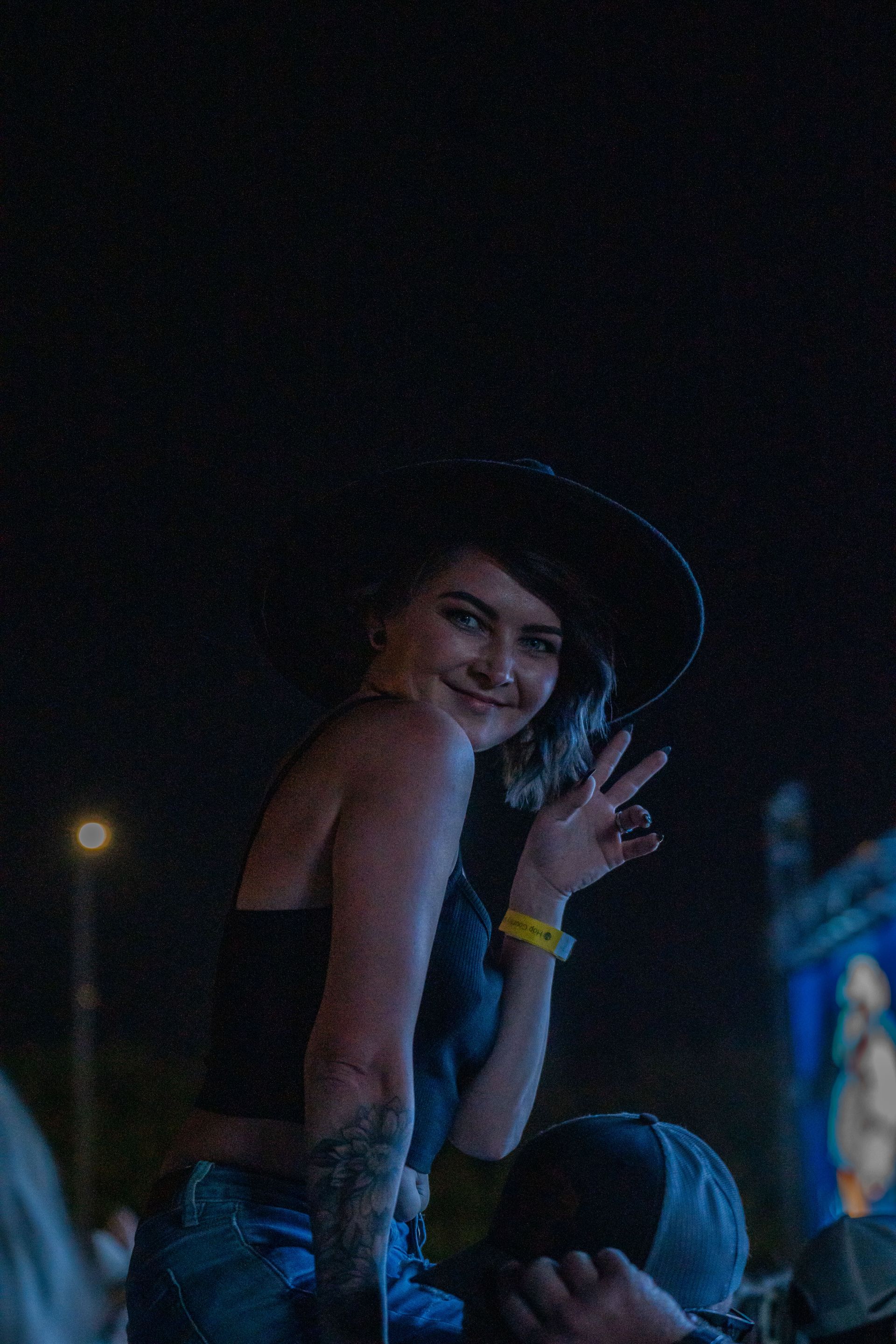 A woman in a hat is waving at the camera at a concert.