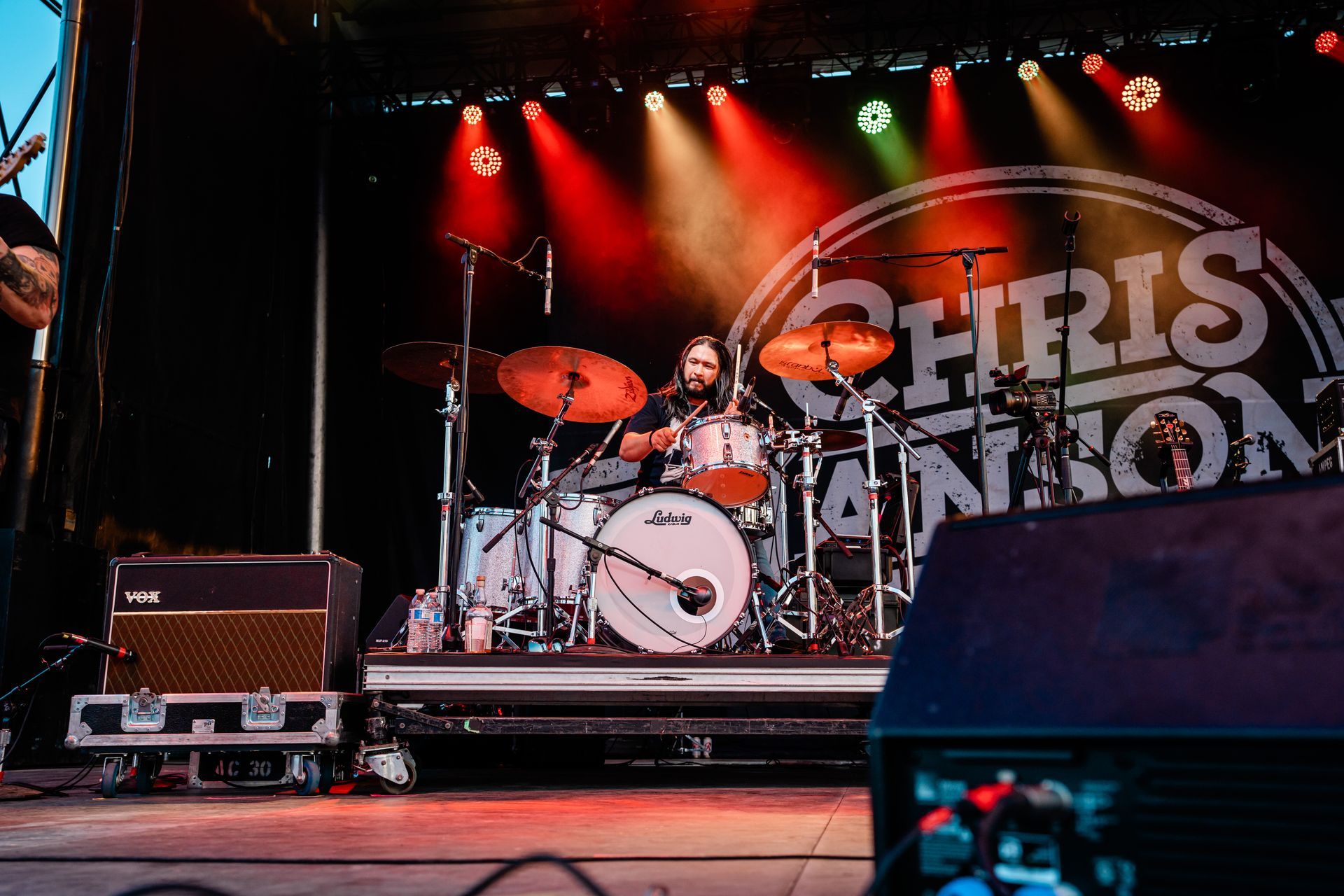 A man is playing drums on a stage in front of a sign that says chris johnson