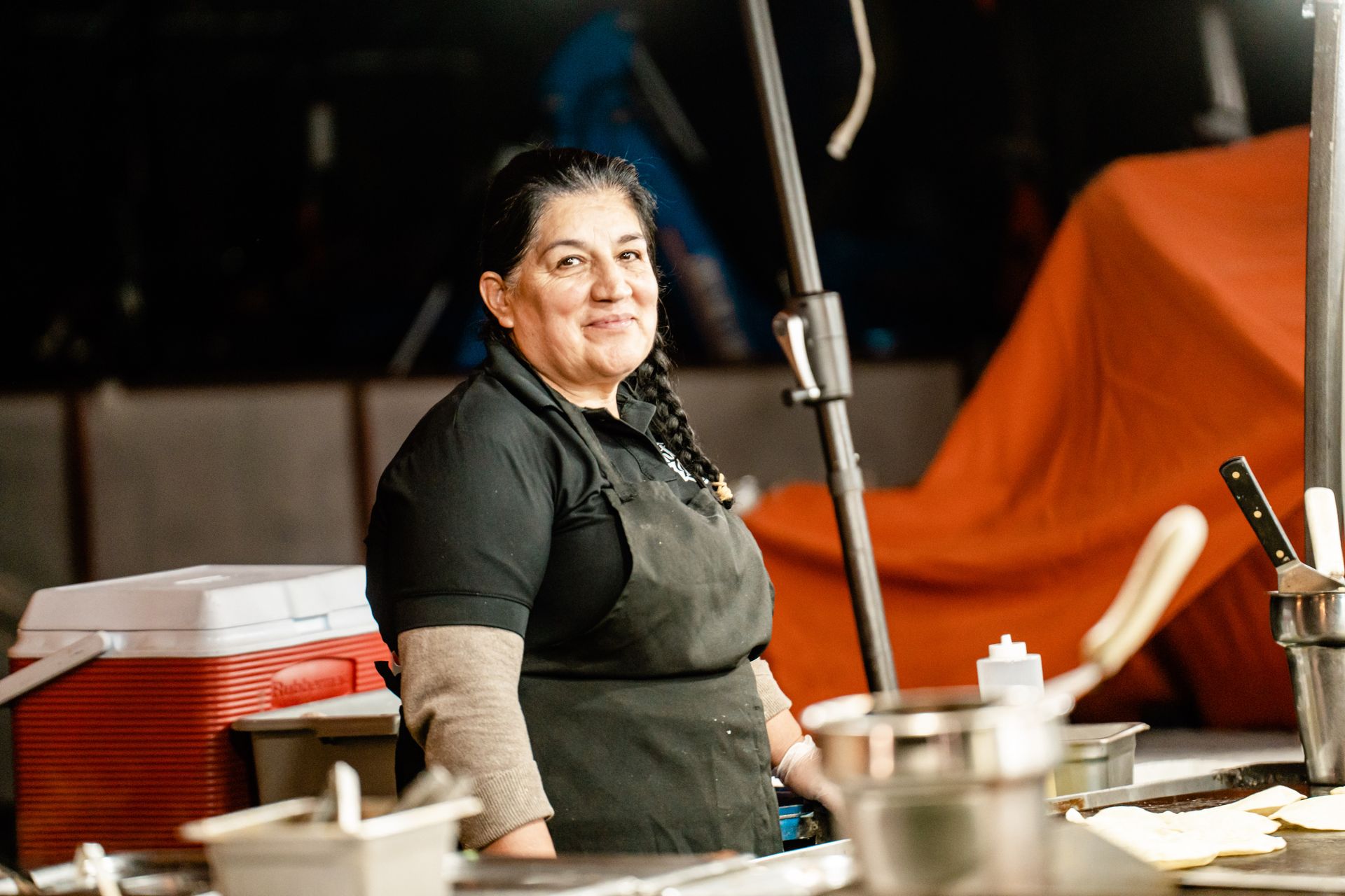A woman in a black apron is standing in front of a kitchen counter.