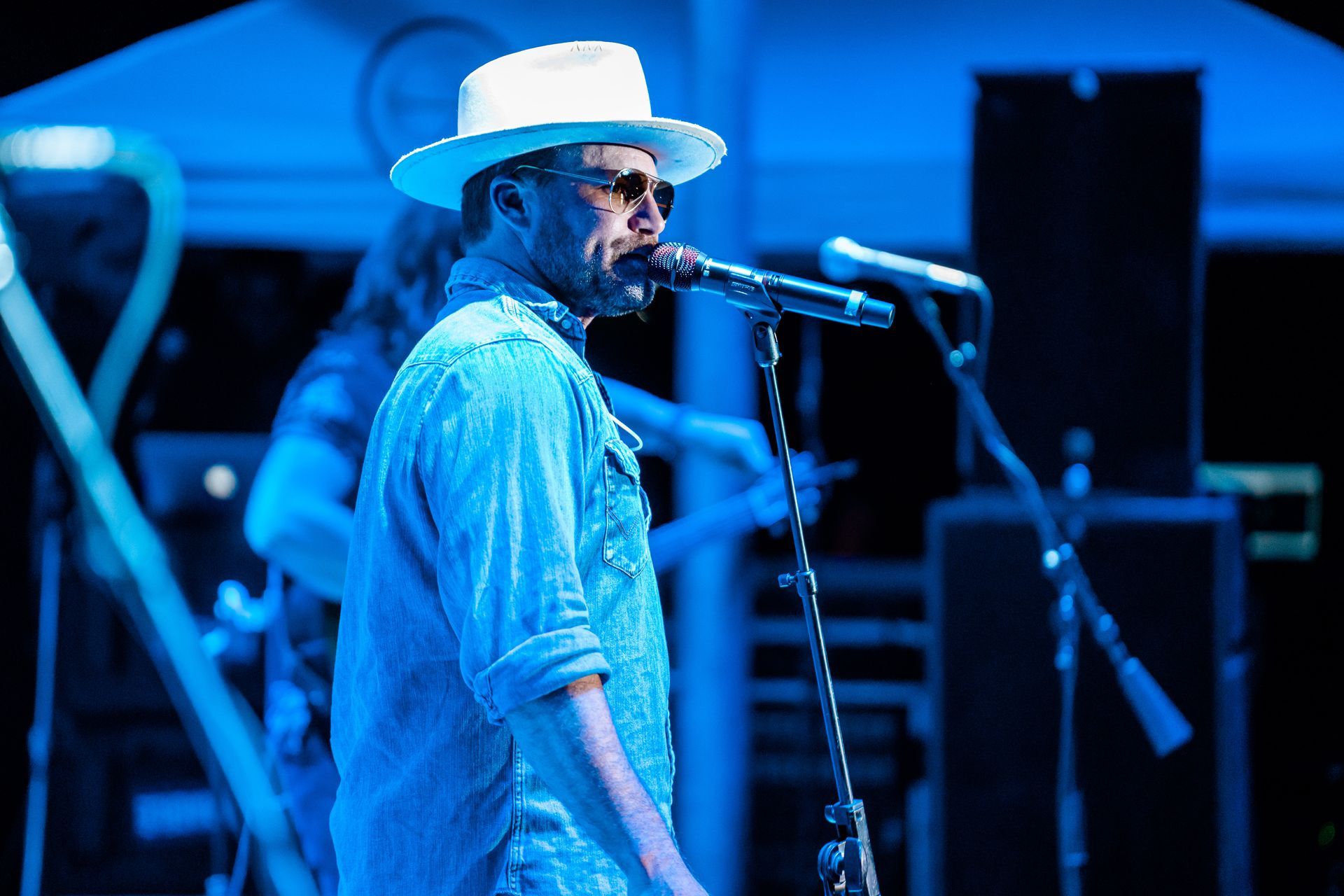 A man in a hat is singing into a microphone on a stage.