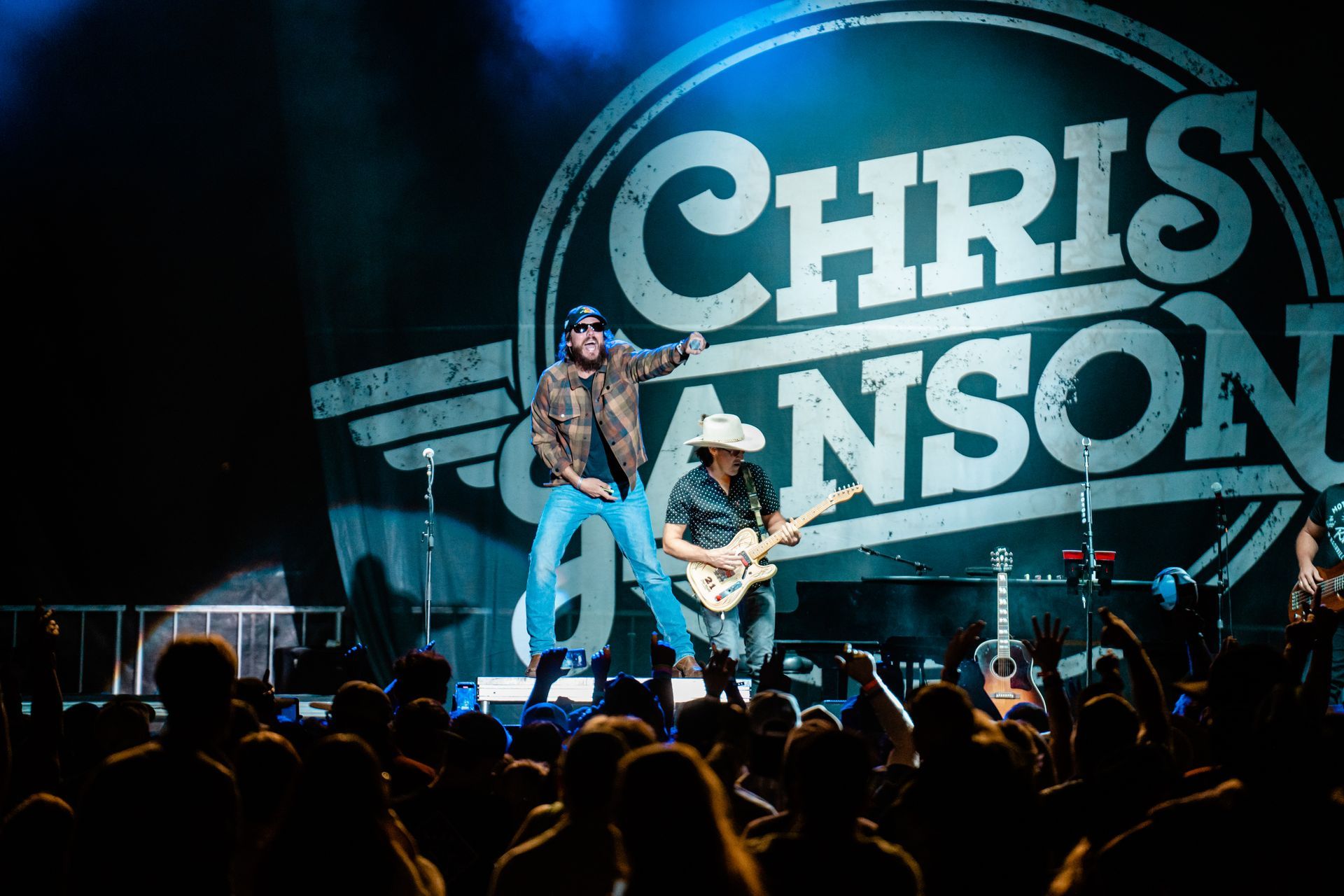 A man is playing a guitar in front of a crowd at a chris fanson concert.