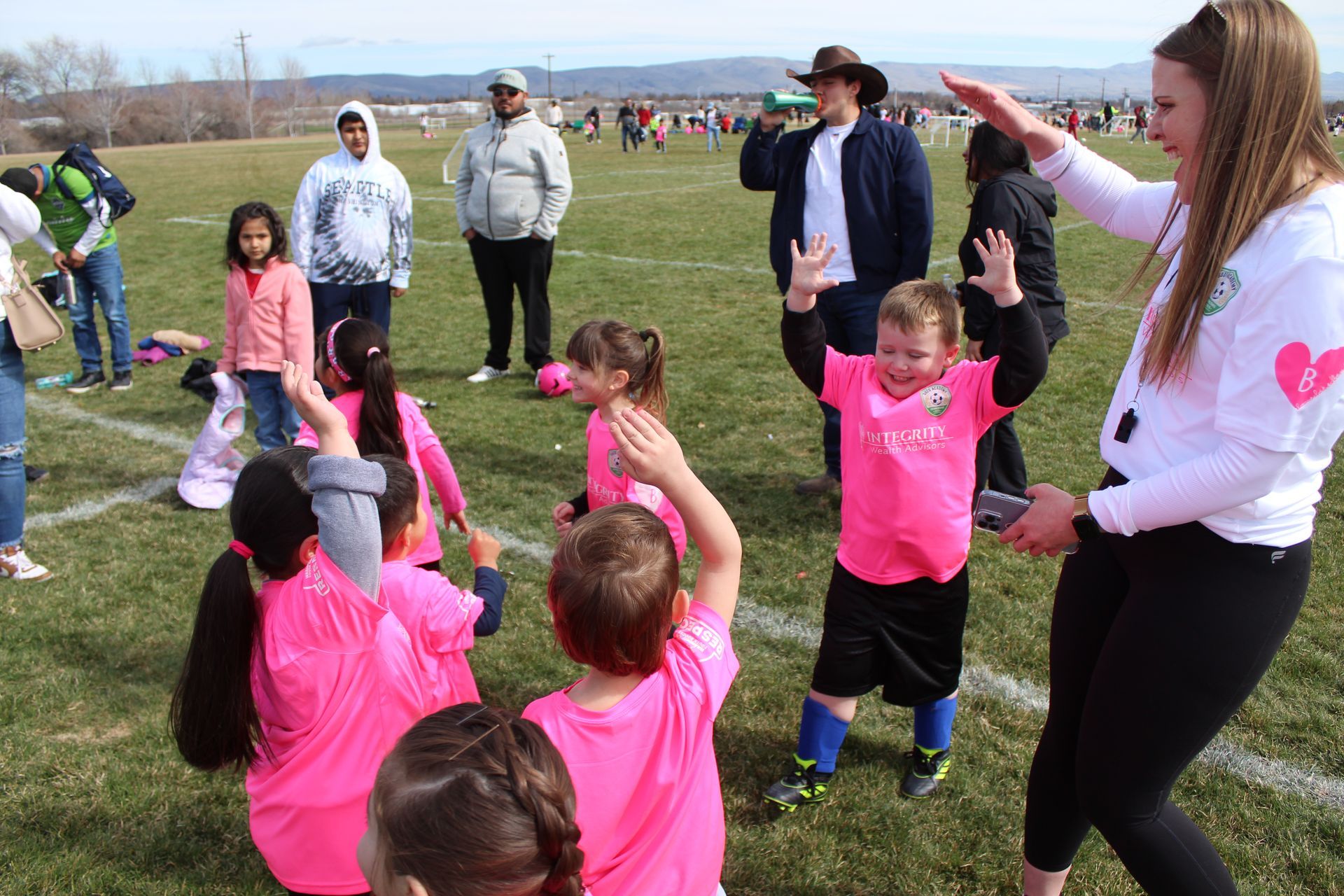 A group of children in pink shirts are playing on a field.