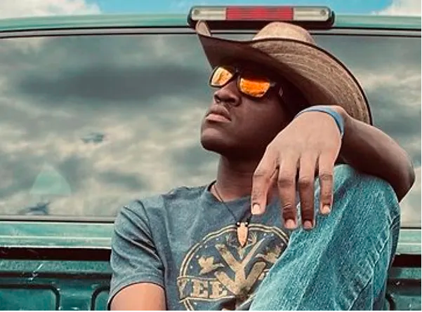 A man wearing a cowboy hat and sunglasses is sitting in the back of a truck.