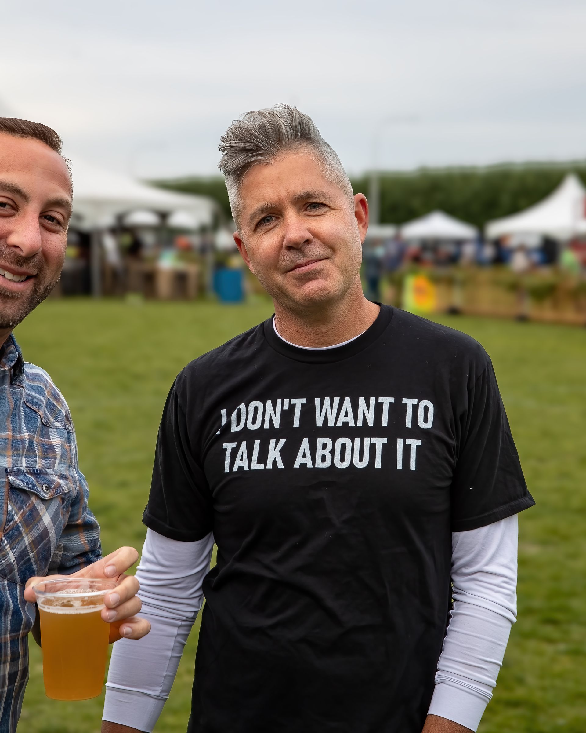 Two men are standing in a field with one wearing a t-shirt that says 