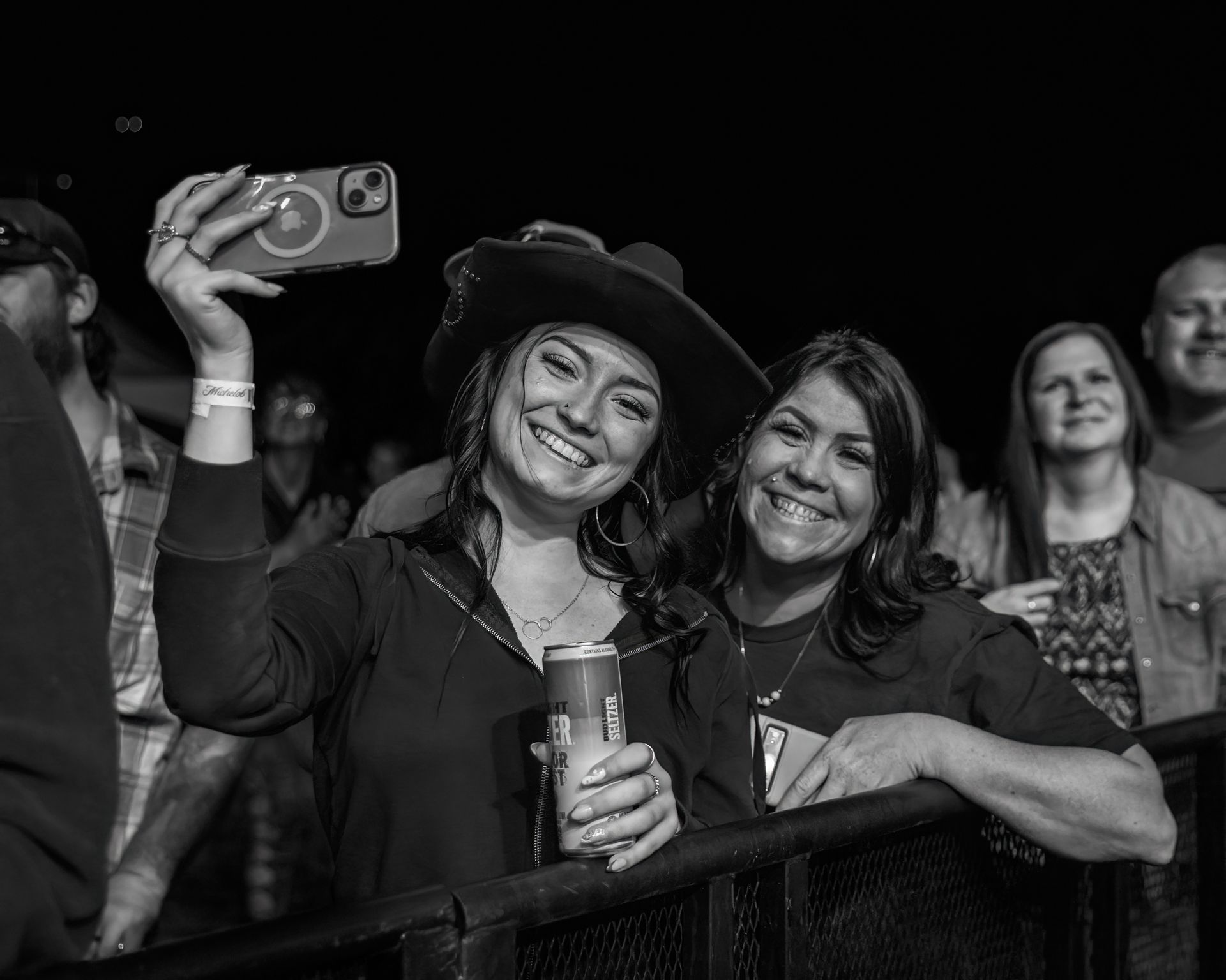 A black and white photo of two women taking a selfie at a concert.