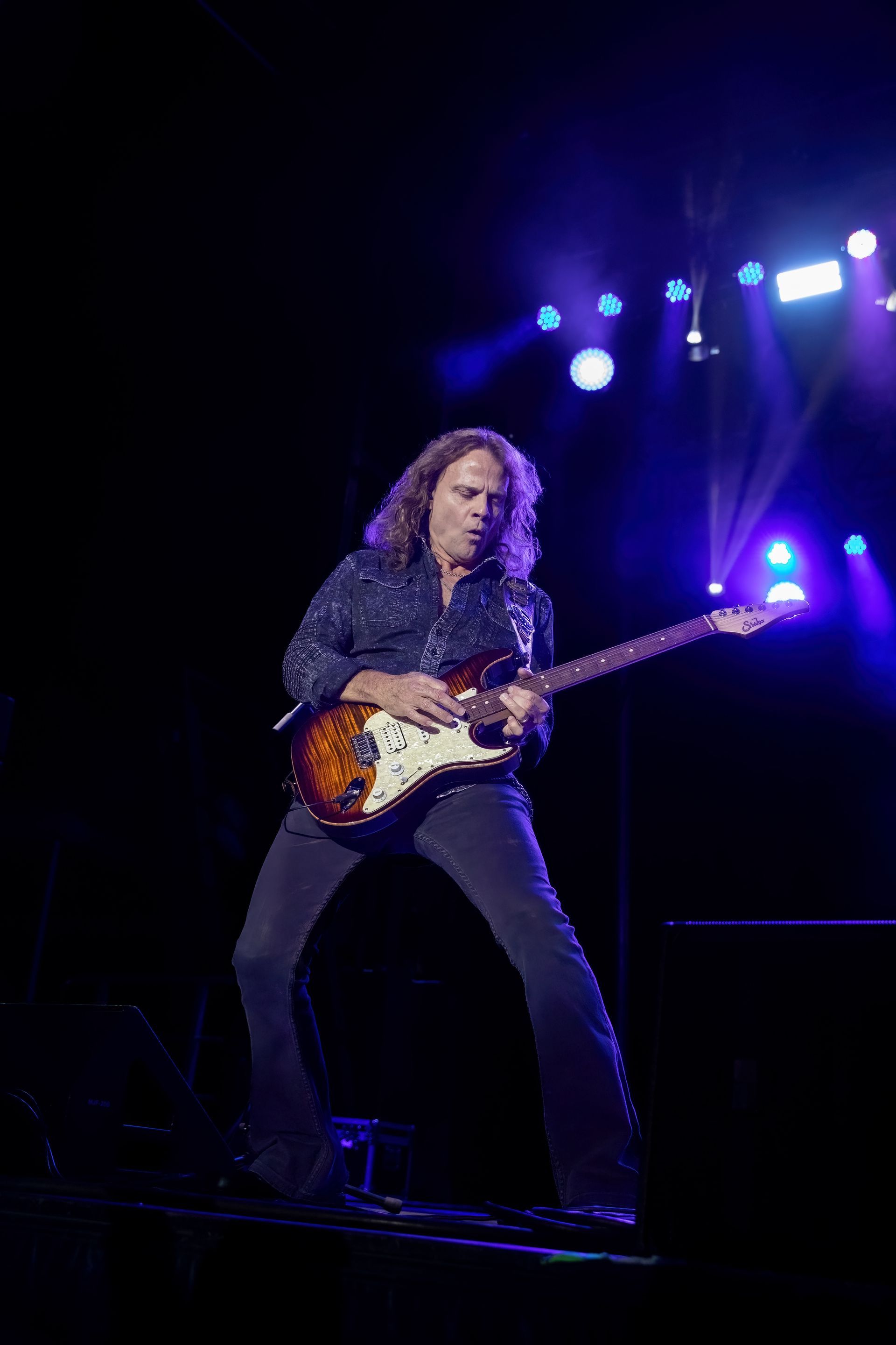 A man is playing a guitar on a stage in the dark.