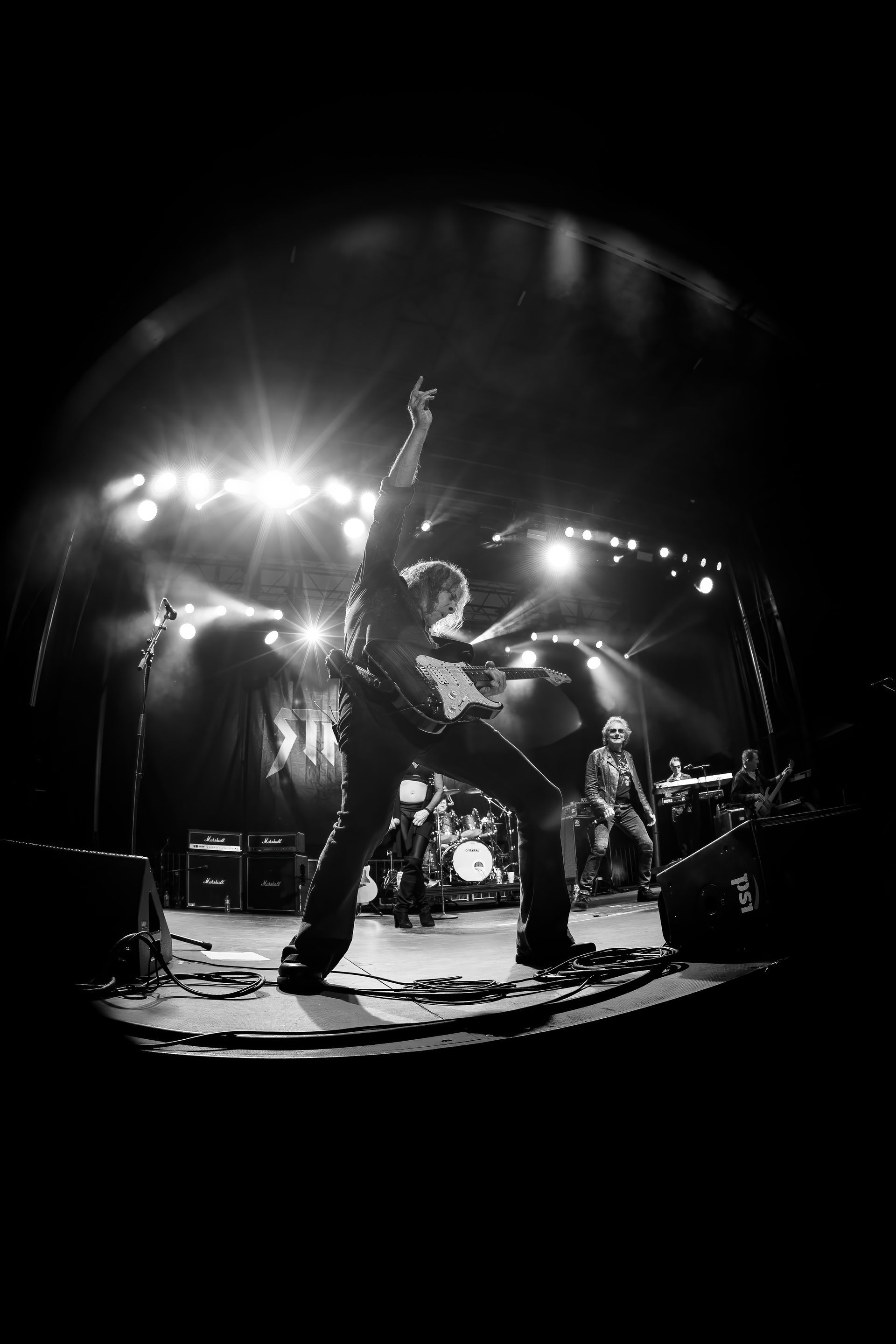 A black and white photo of a man playing a guitar on a stage.