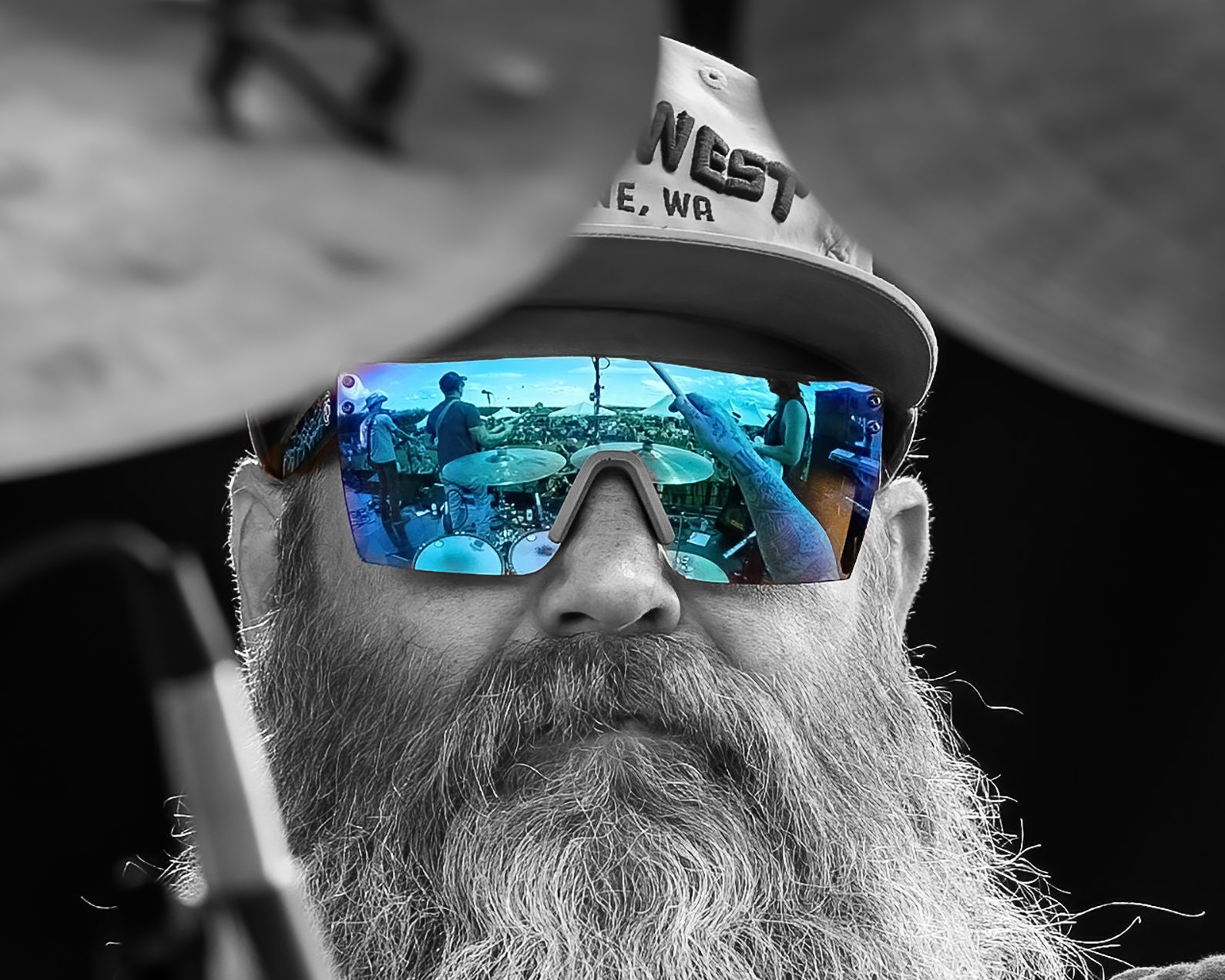 A man with a beard wearing sunglasses and a hat that says west