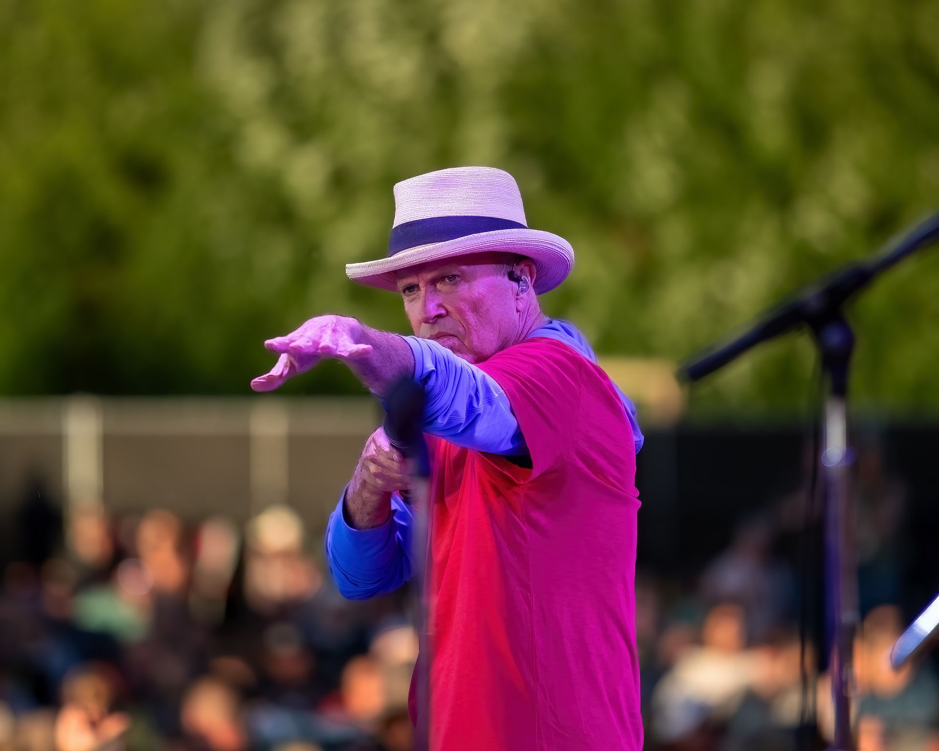 A man wearing a hat and a pink shirt is standing in front of a microphone.