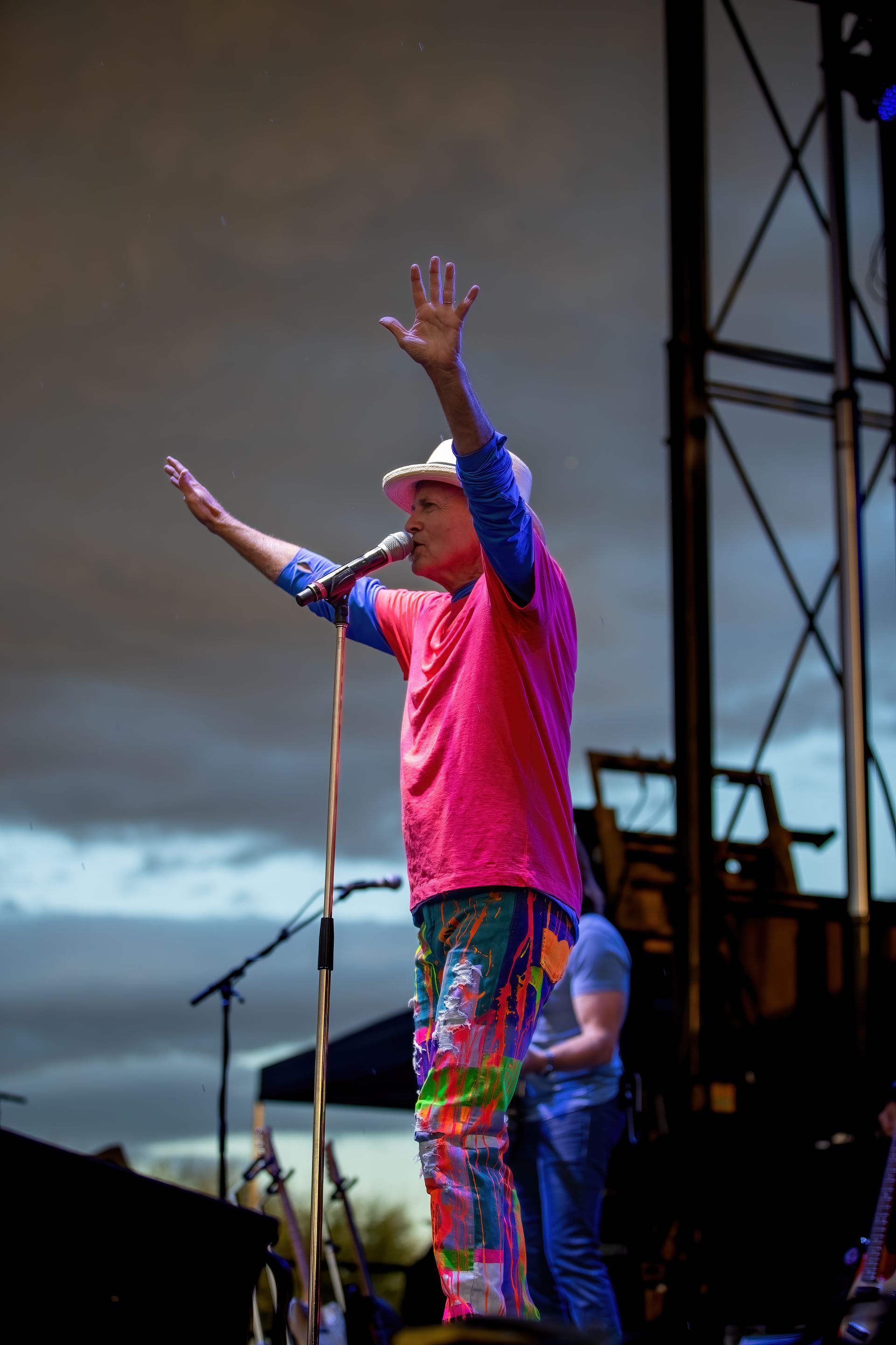 A man in a pink shirt is singing into a microphone on a stage