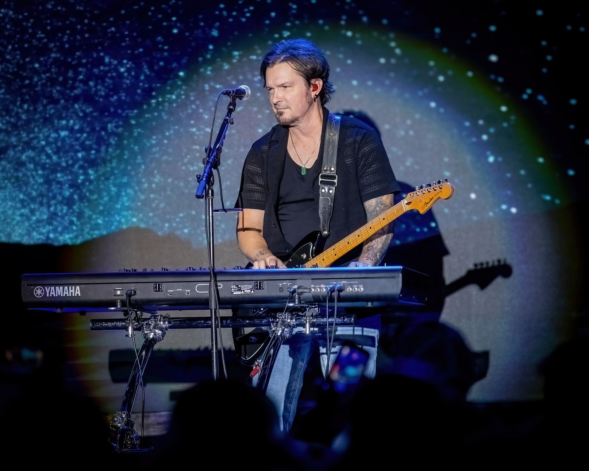 A man is playing a keyboard and singing into a microphone on a stage.