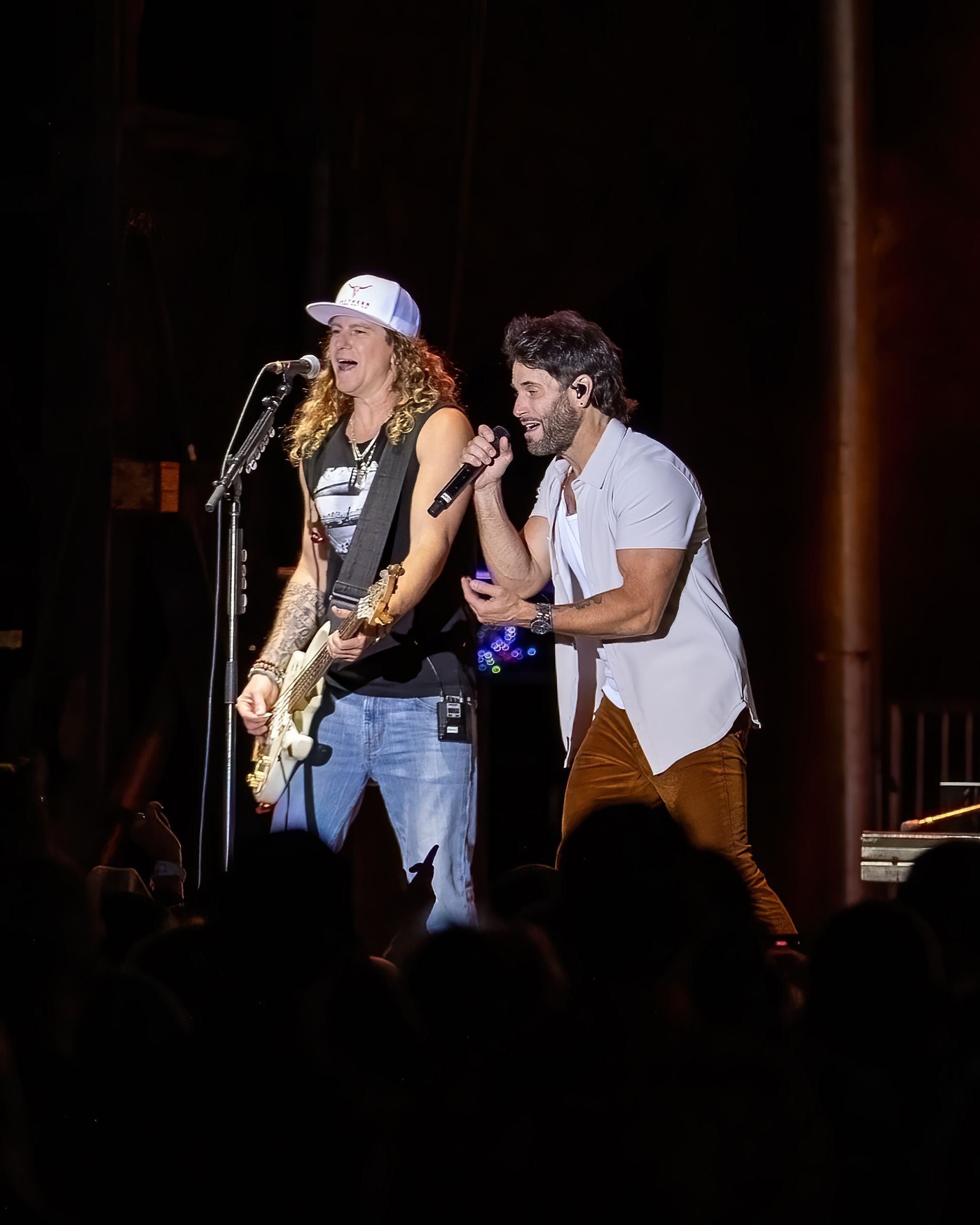 Two men are singing and playing guitar on a stage in front of a crowd.