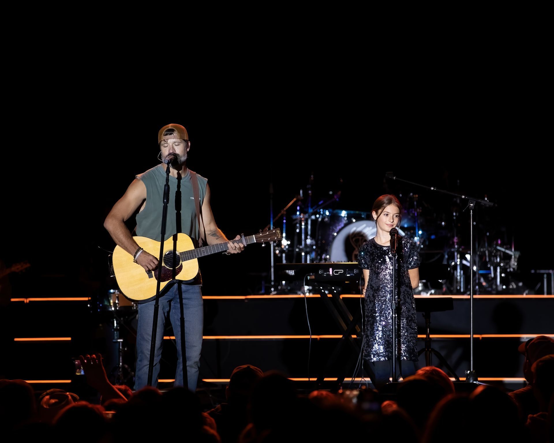 A man playing a guitar and a girl singing on stage