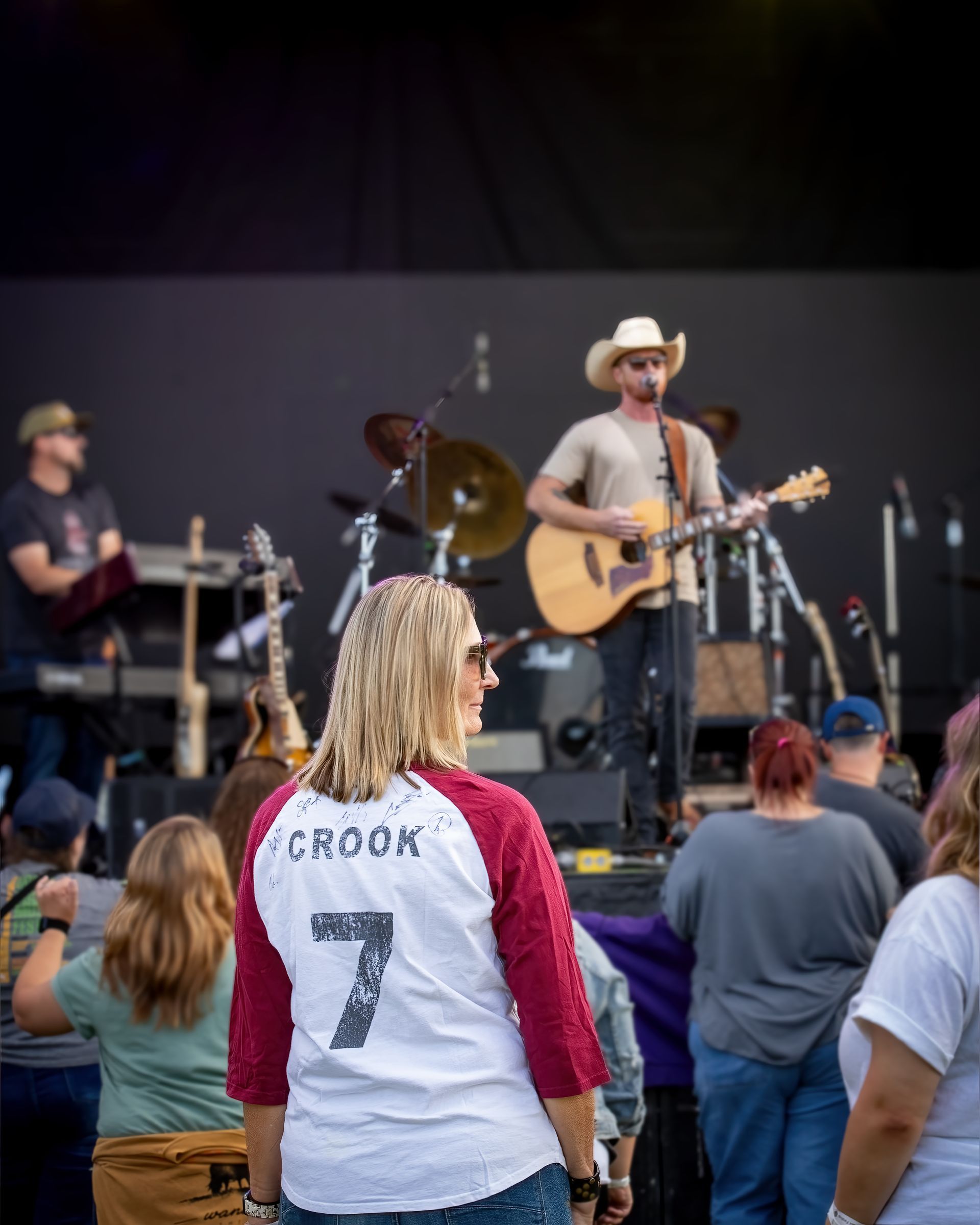 A woman wearing a crook shirt is watching a man play a guitar on stage.