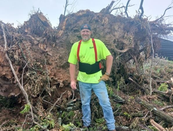 A man is standing in front of a pile of fallen trees.