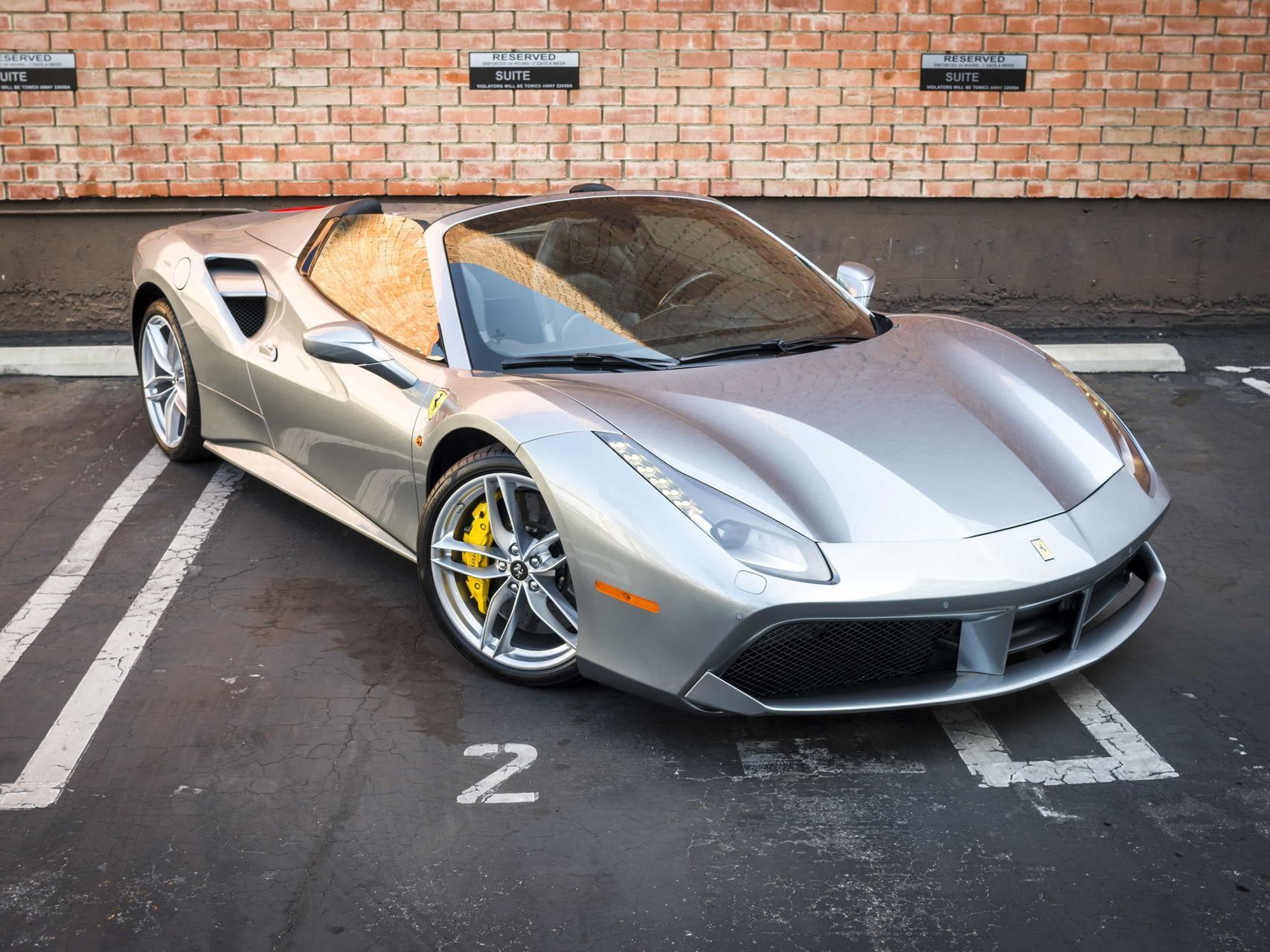 Silver Ferrari convertible parked in a parking space, yellow brake calipers.
